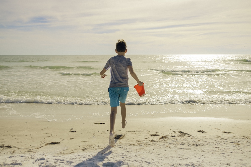 young boy running into the gulf with sand pail