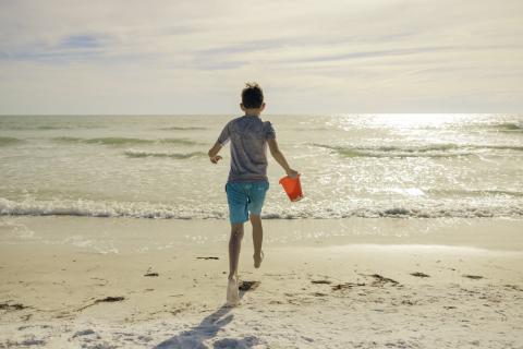 boy running with sand pail into ocean