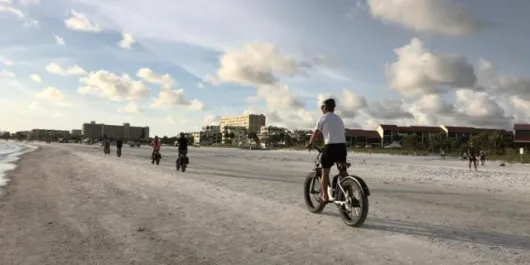 people riding bikes on the beach at sunset