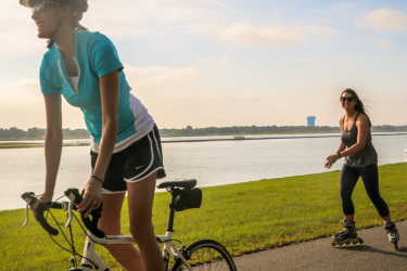 Woman biking and woman roller blading at a park on the water