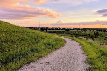 Gravel road around a hill showing clouds at sunset