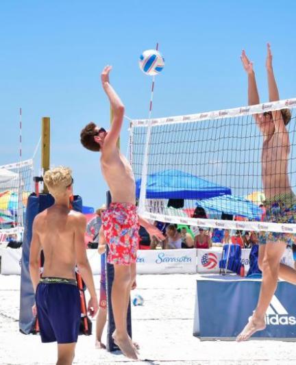 Guys jumping up over volleyball net during game.