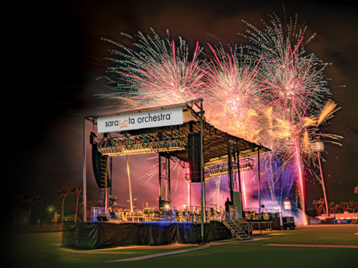Fireworks going off in the sky behind the Sarasota Orchestra stage on the baseball field