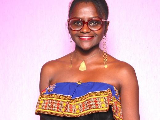 Woman from Kenya smiles at camera with hair in high bun and beautiful black dress on with purple and frills at the top.