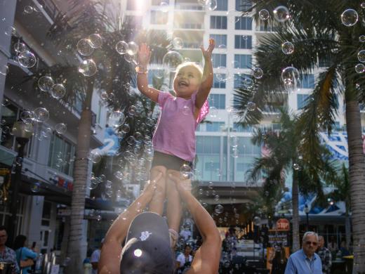 Little girl reaches towards bubbles in the sky