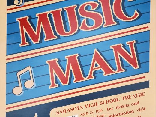 Vibrant retro-style poster for the musical "The Music Man" presented by Sarasota High School Theatre. The design features a blue background with musical staff lines, a large bold red title, and musical notes (treble clef and eighth notes) scattered around. Below the title, event details are listed: performances at Sarasota High School Theatre on April 22, 23, and 24 at 7pm, and April 25 at 2pm and 7pm. A QR code is included along with ticket and information details directing to shstheater.com.