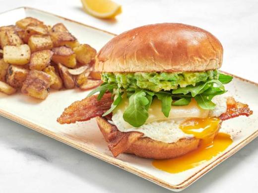 Elevated Egg Sandwich - Fresh, over-easy cage-free egg with bacon, Gruyere cheese, fresh smashed avocado, mayo and lemon-dressed arugula on a brioche bun. Served with fresh, seasoned potatoes. Photo 2