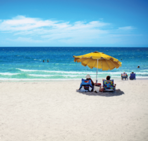 People under a yellow umbrella on Siesta Beach by the water.