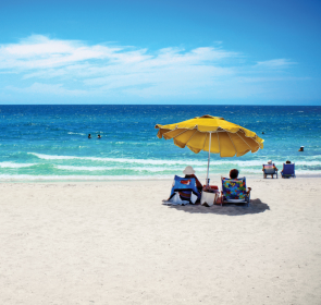 2  people under a yellow beach umbrella looking at the shore