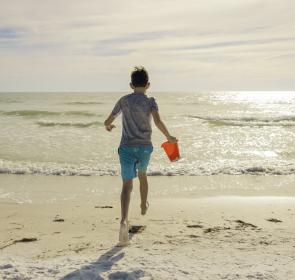 boy running with sand pail into ocean