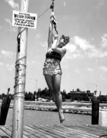 Tarpon queen Barbara Glidden poses for a photograph while hanging from a weighing device - Sarasota, Florida 1962.jpg