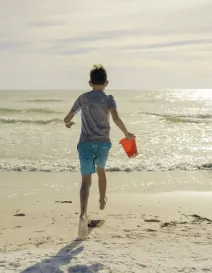 boy running with sand pail into ocean