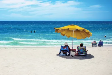 2  people under a yellow beach umbrella looking at the shore