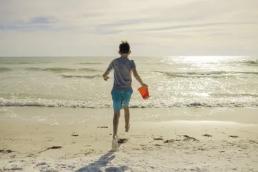 boy running with sand pail into ocean