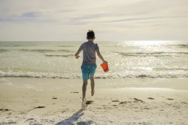 boy running with sand pail into ocean