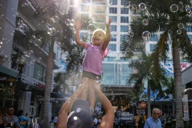 Little girl reaches towards bubbles in the sky
