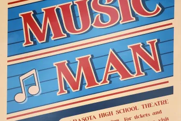 Vibrant retro-style poster for the musical "The Music Man" presented by Sarasota High School Theatre. The design features a blue background with musical staff lines, a large bold red title, and musical notes (treble clef and eighth notes) scattered around. Below the title, event details are listed: performances at Sarasota High School Theatre on April 22, 23, and 24 at 7pm, and April 25 at 2pm and 7pm. A QR code is included along with ticket and information details directing to shstheater.com.
